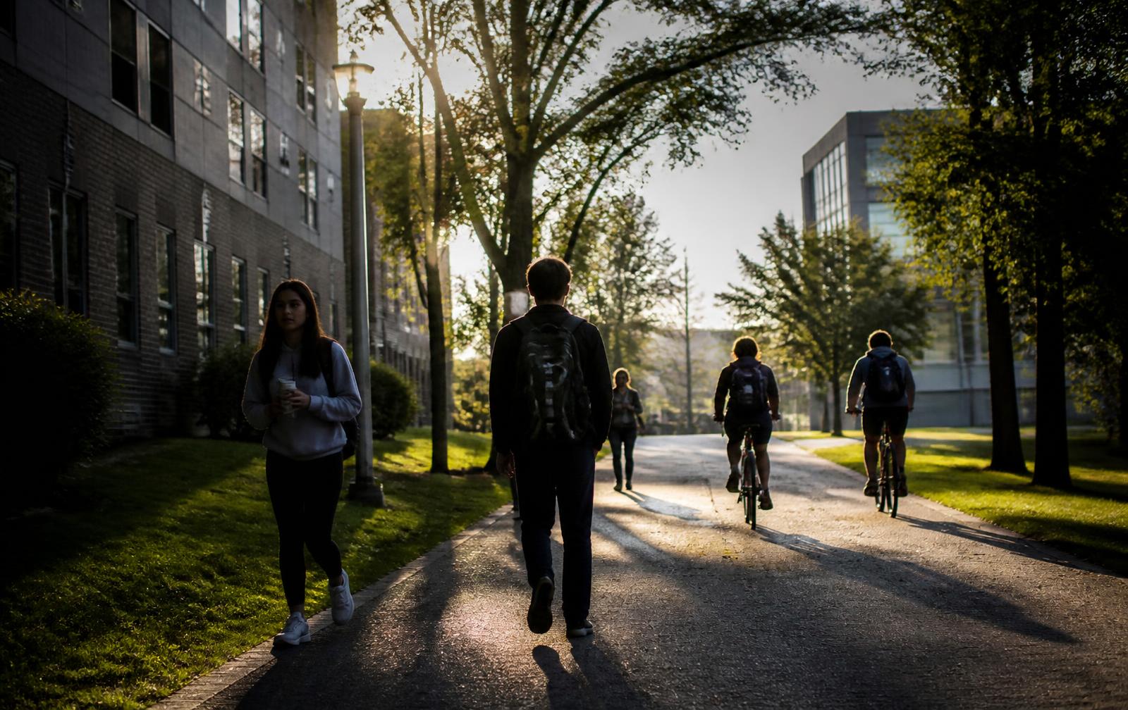 Students walking and biking between a housing community and campus at sunrise